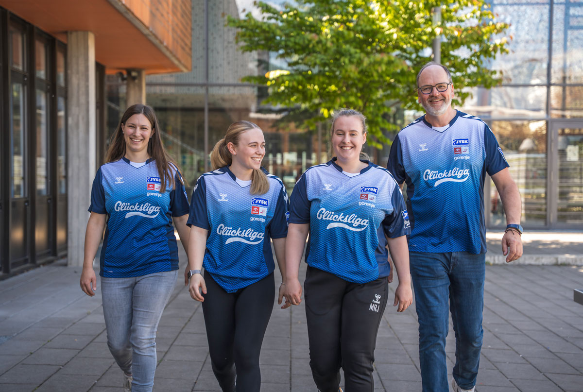 Janine, Mia, Maria und Andreas gehen nebeneinander auf die Kamera zu. Alle tragen blaue Glücksliga-Trikots